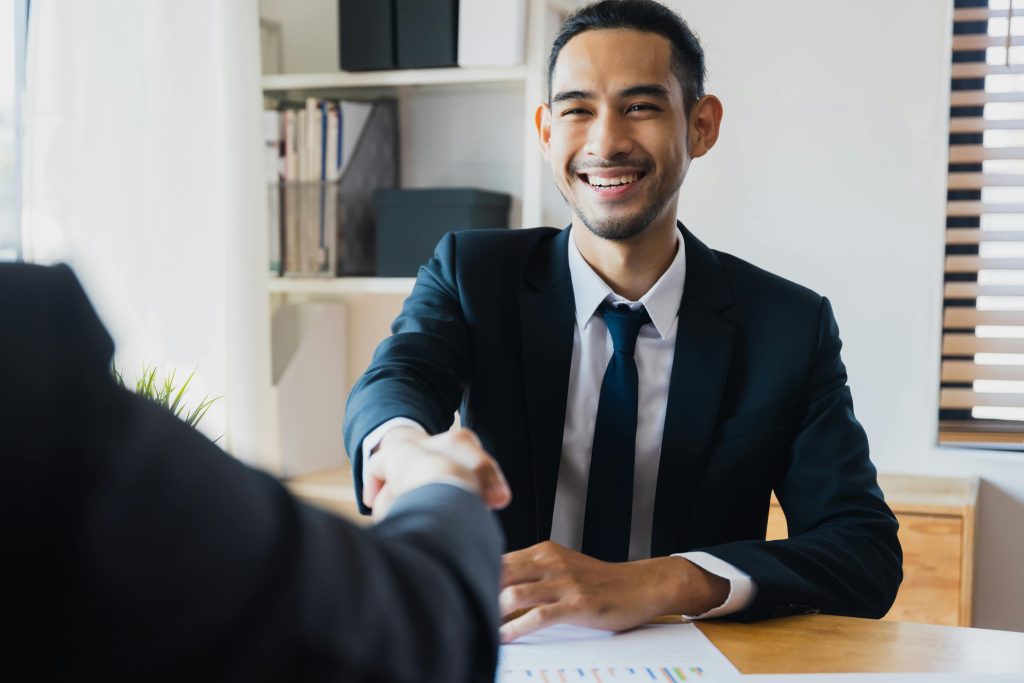 pexels photo 12885861 12885861 Confident businessman in suit shaking hands at office desk, symbolizing successful partnership.